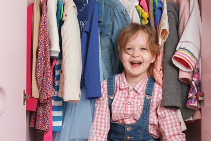 Ein lachendes Kind sitzt in einem Kleiderschrank