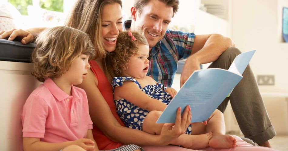 Ein Elternpaar liest gemeinsam mit seinen zwei Kindern ein Kinderbuch und sehen dabei glücklich aus.