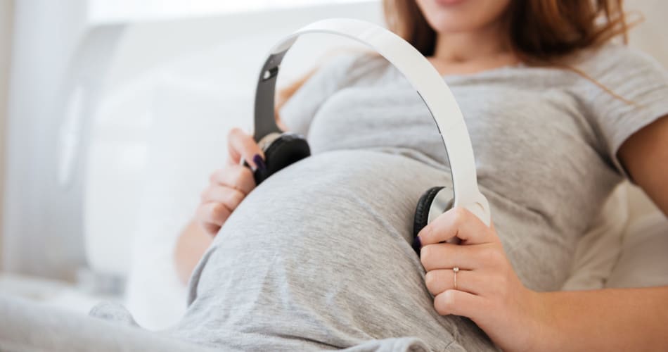 Eine Schwangere Frau, die Kopfhörer auf ihr Bauch hält, um ihrem Baby im Bauch Musik vorzuspielen.