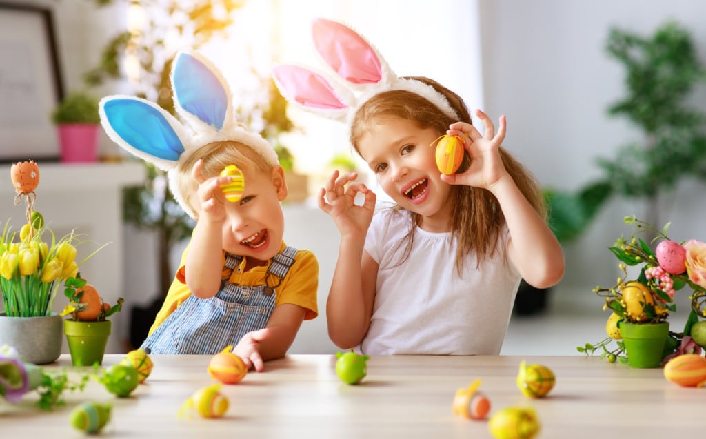 Zwei Kleinkinder halten bemalte Ostereier in die Kamera und lächeln.