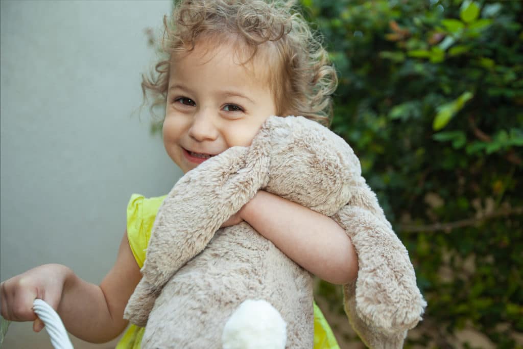 Ein Mädchen hält ein Osterhasen-Kuscheltier im Arm und lächelt in die Kamera.