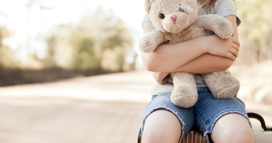 Ein kleines Mädchen mit einem Teddy-Bären im Arm. Man sieht das Kind vom Hals abwärts.