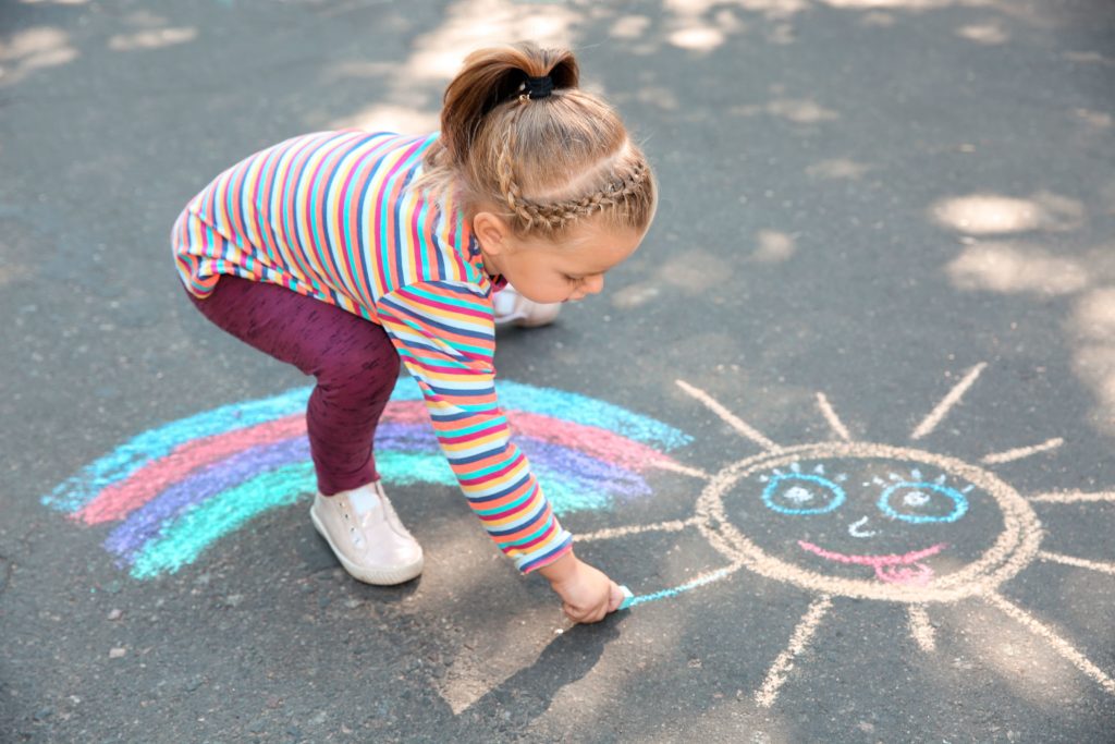 Ein Mädchen malt mit Kreide zu Hause auf der Straße.