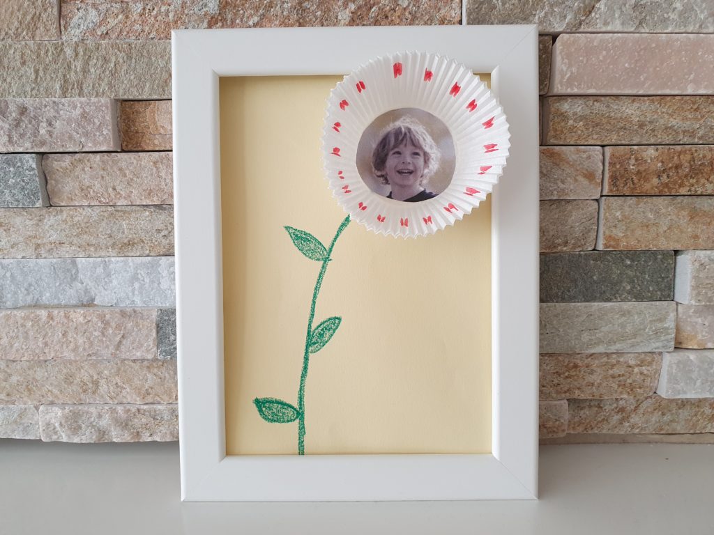 Ein Bilderrahmen mit einer Fotoblume aus einem Muffinförmchen von Kindern als Geschenk für Mama selbstgemacht.