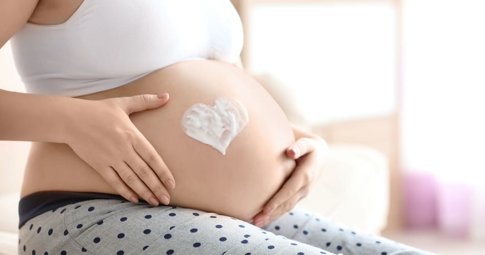 Eine hochschwangere Frau pflegt ihren Babybauch mit Creme.