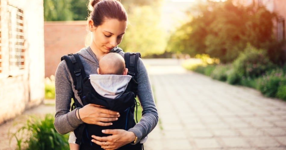 Eine Mutter trägt ihr Baby in einer Babytrage - Beispielbild für Babytrage-Tipps.