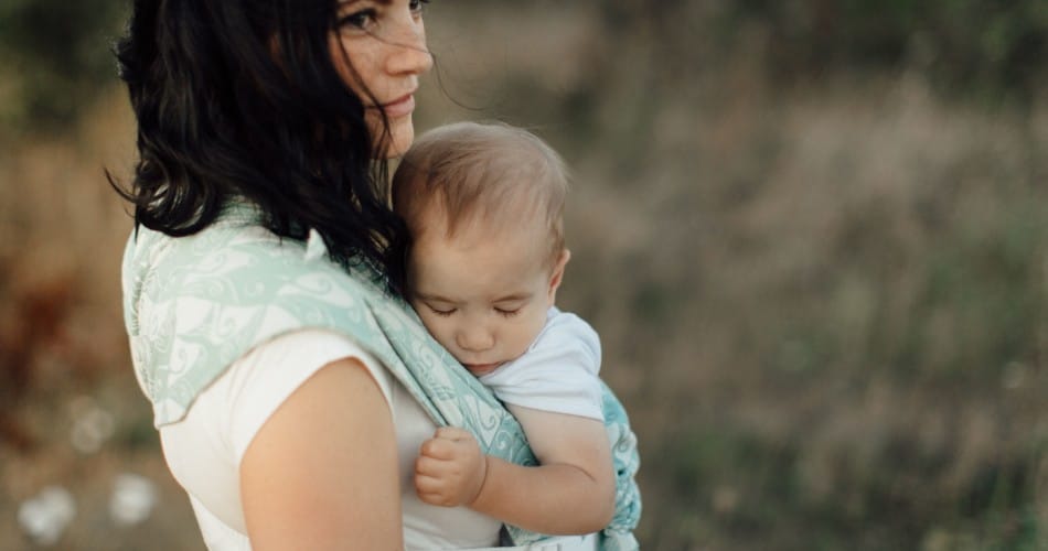 Eine Mutter trägt ihr Baby in einer Tragehilfe - Titelbild zu bindungsorientierter Erziehung.