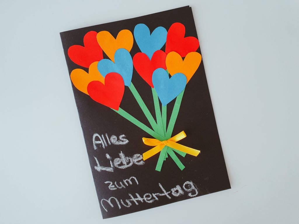 Eine schwarze Karte mit einem Blumenstrauß aus bunten Herzen als Geschenk von Kindern zum Muttertag gebastelt.