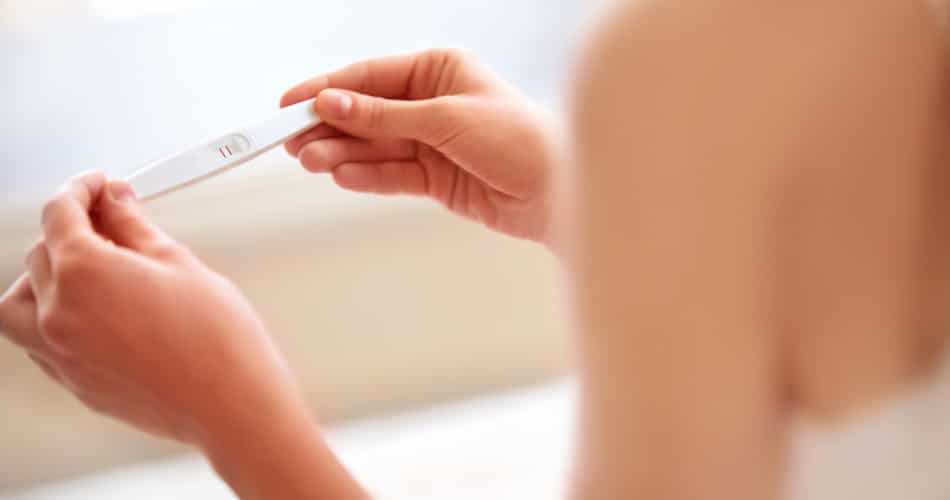Schwangere Frau hält Test und fragt sich, was in der frühen Schwangerschaft schadet.