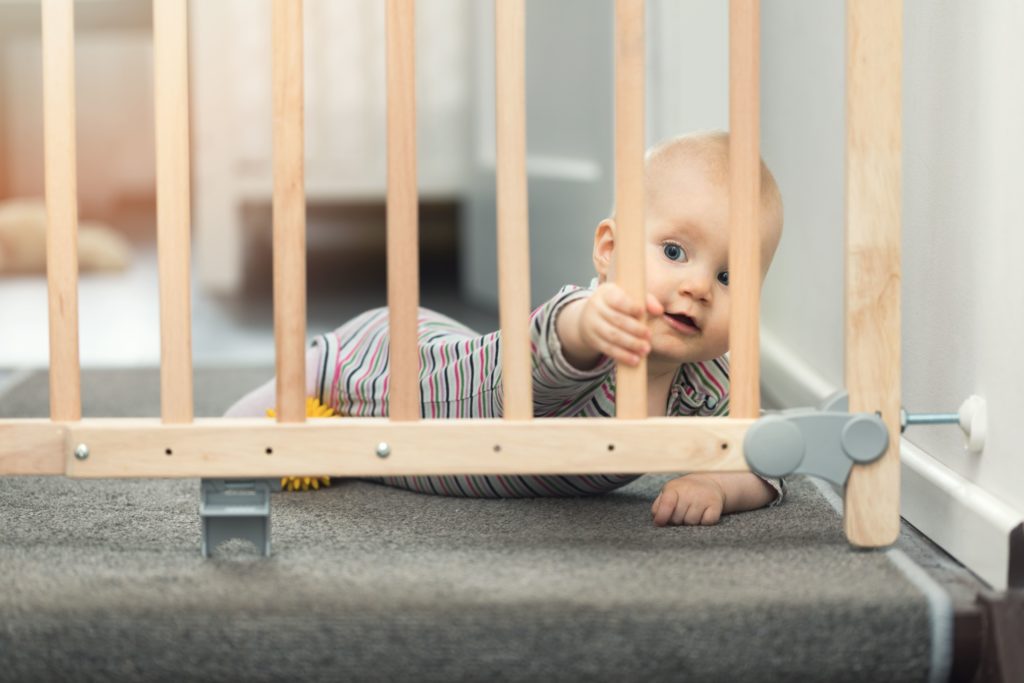 Ein Baby greift nach einem Treppenschutzgitter.