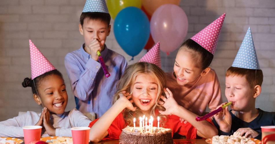 Auf dem Bild schauen fünf Kinder fröhlich auf einen Geburtstagskuchen herab.
