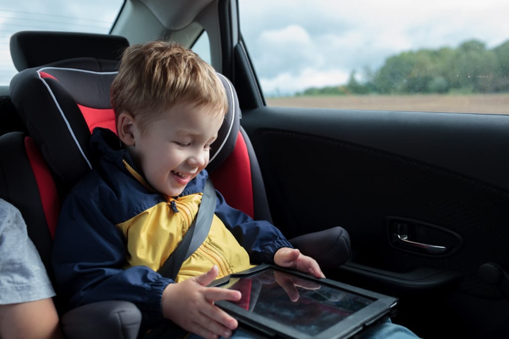 Ein Kleinkind mit einem Tablet in der Hand im Auto.