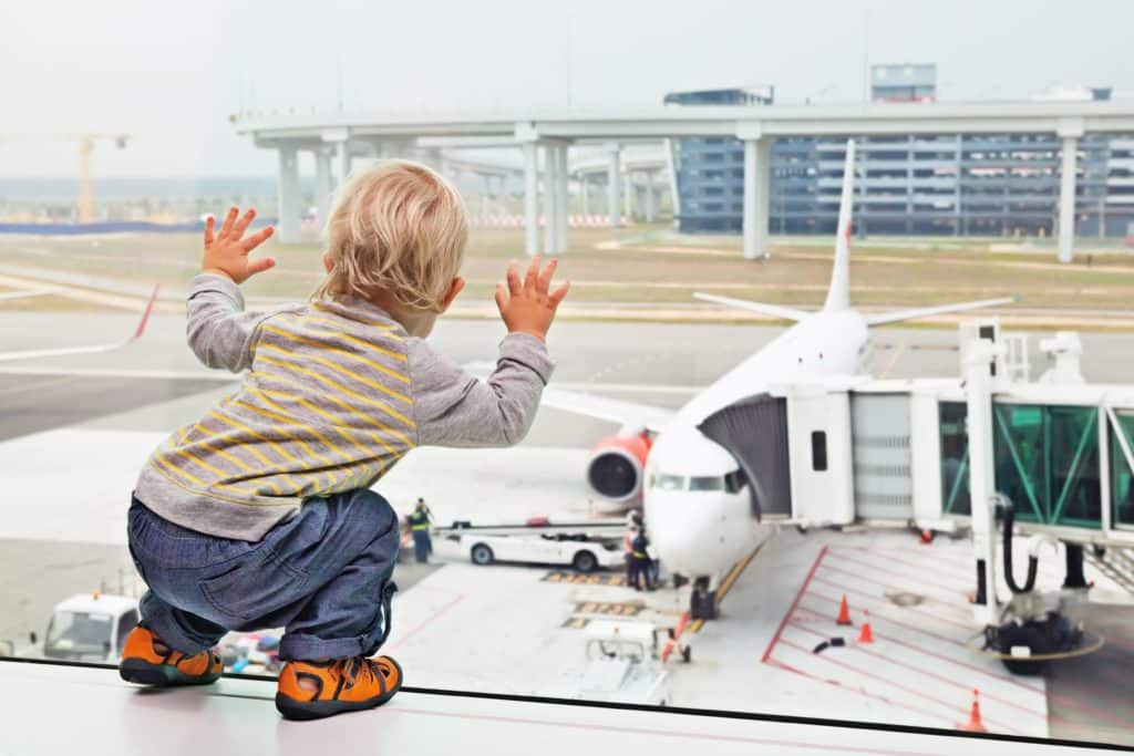 Baby / Kleinkind steht am Flughafen und beobachtet ein Flugzeug.