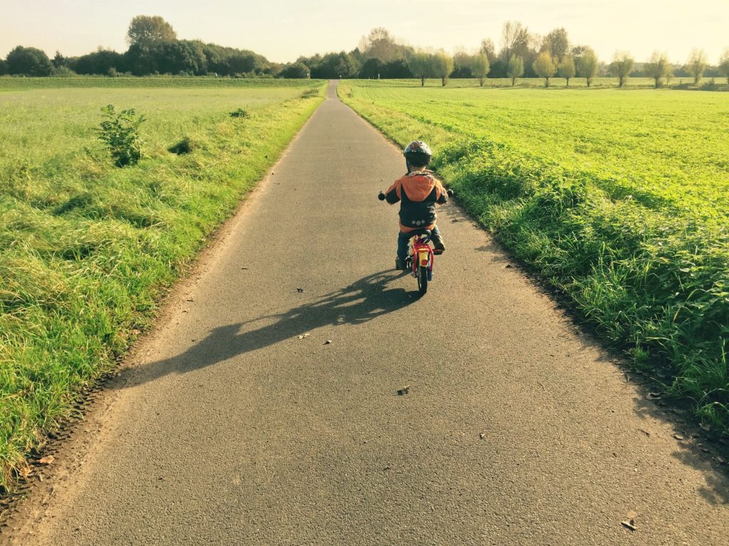 Ein Kind lernt auf einem Feldweg das Fahrradfahren.