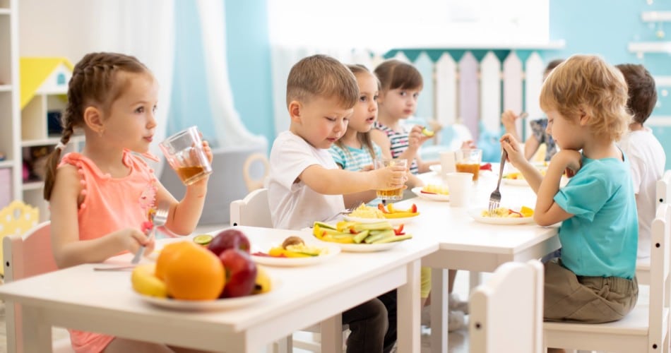 Kinder sitzen am Esstisch in der Kita uns ernähren sich gesund