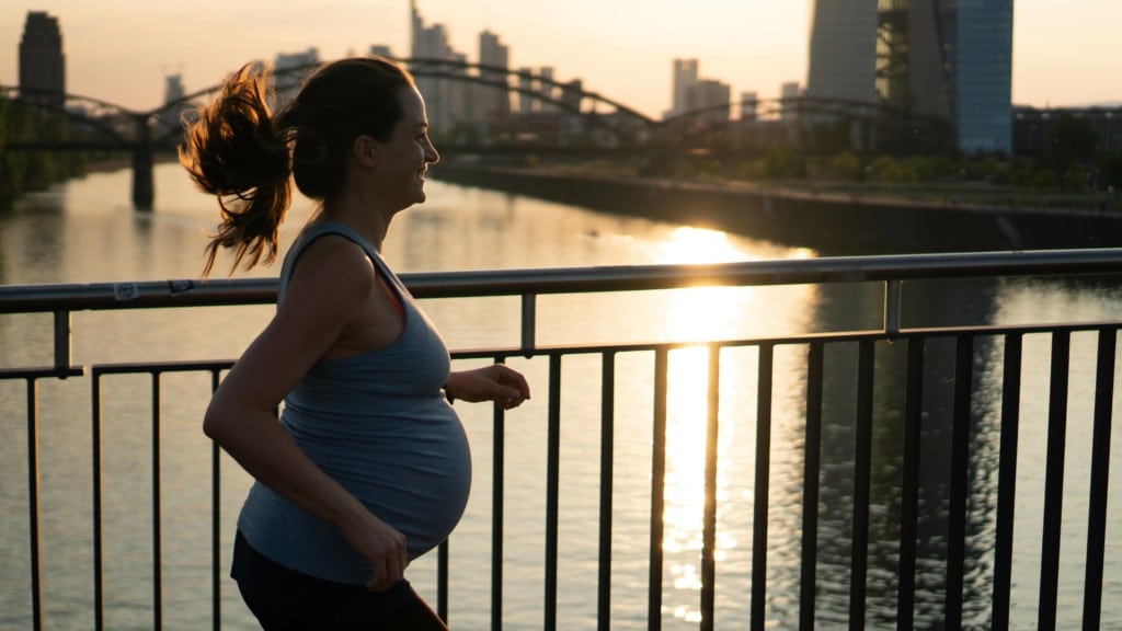 EIne schwangere Frau beim Joggen auf einer Brücke