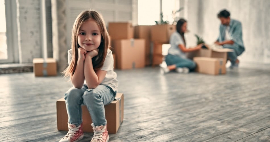 Der Umzug einer Familie mit Kindern: Ein Mädchen sitzt auf einem Umzugskarton und lächelt in die Kamera