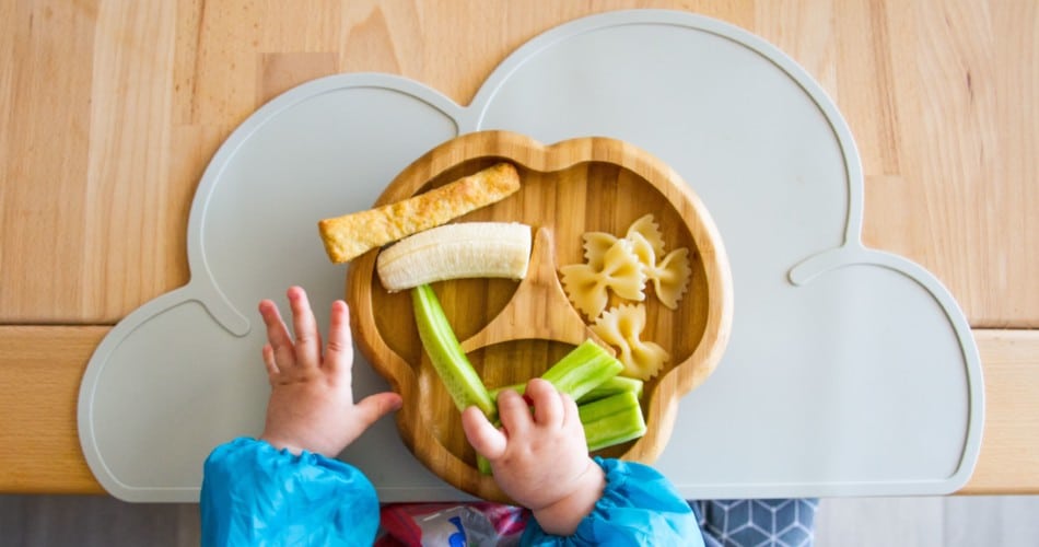 Kinderhände, die nach Lebensmitteln auf einem Teller greifen. Titelbild für Artikel über BLW mit Infos, ab wann man BLW ausprobieren kann.
