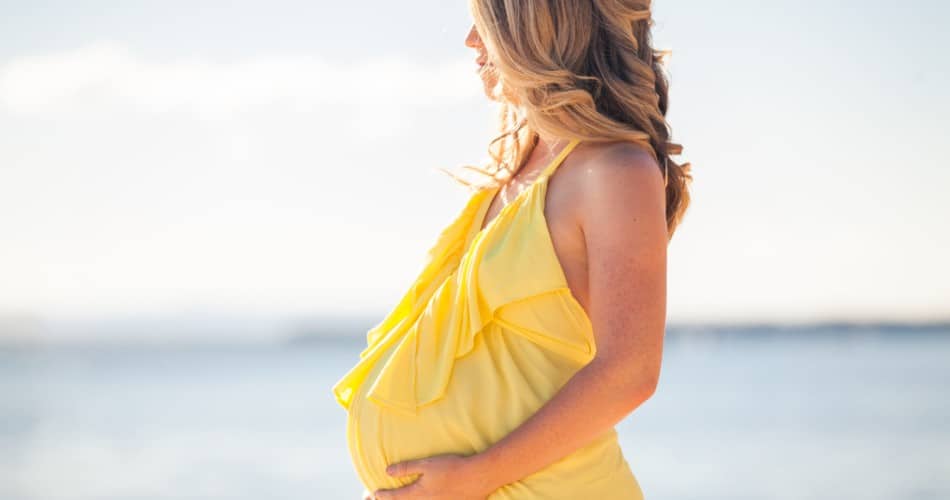 Eine Frau in einem gelben Kleid, die im Sommer schwanger ist.