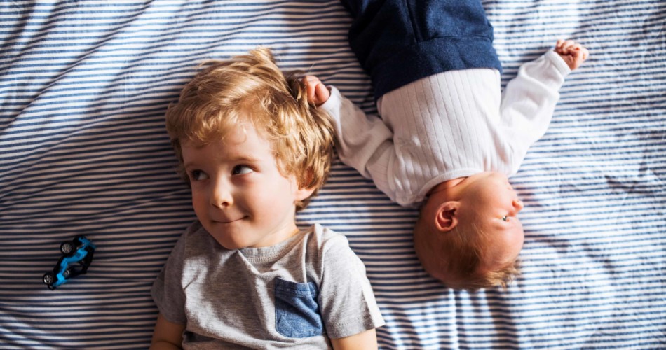 Eifersucht unter jungen Geschwistern: Kleinkind und Baby lieben zusammen auf einem Bett.