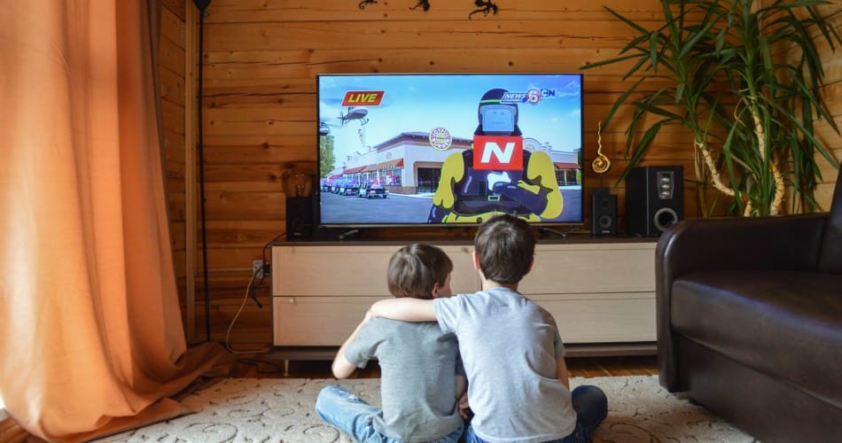 Fernsehkonsum: Kinder fernsehen. Man sieht sie von hinten. Sie sitzen auf dem Boden und schauen auf das TV-Gerät.