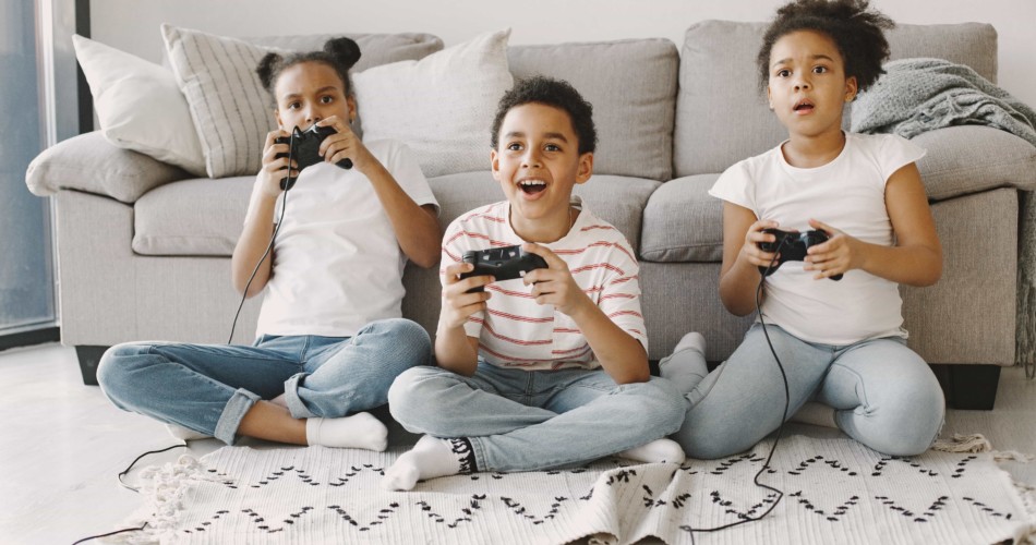 Drei Kinder spielen Videospiele an einer Konsole.