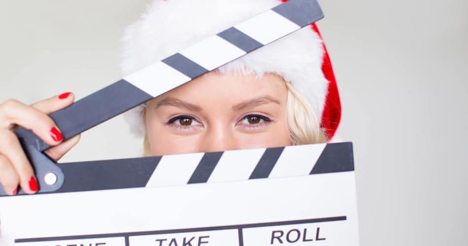 Close-Up von einer Frau, die eine Filmklappe vor ihr Gesicht hält und eine Weihnachtsmütze trägt.