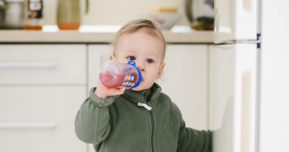 Kleiner Junge trinkt Tee für Babys aus der Flasche.