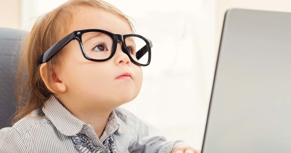 Ein Kleinkind mit Brille sitzt vor dem Bildschirm eines Laptops und schaut darauf.