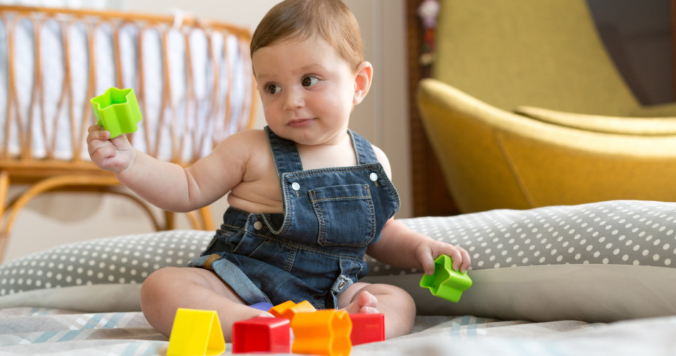 8 Monate altes Baby spielt sitzend mit Bausteinen