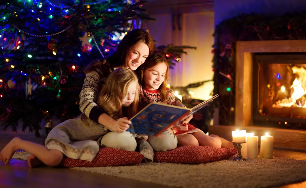 Eine Mutter liest ihren Töchtern in der Adventszeit ein Weihnachtsbuch vor.