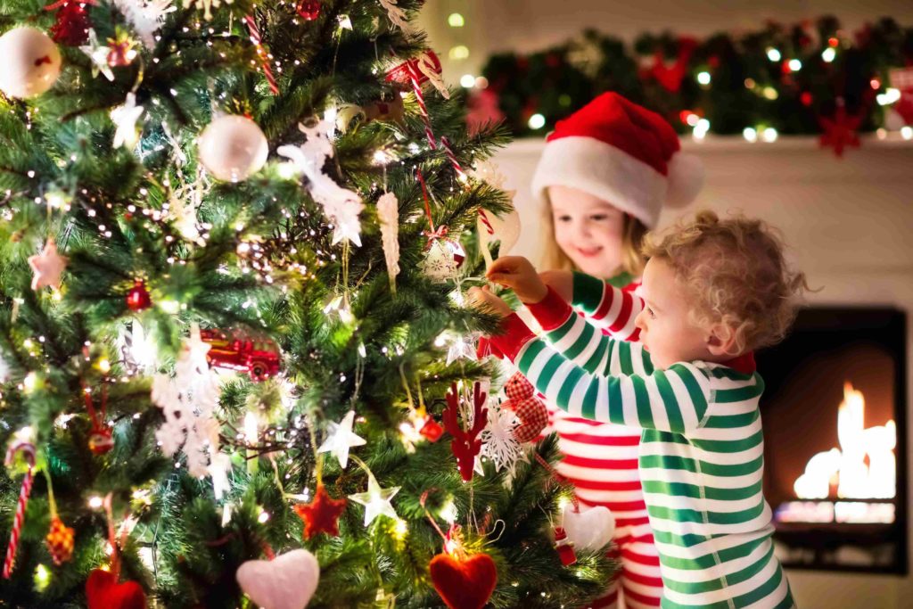 Zwei kleine Kinder schmücken und gestalten in der Adventszeit den Weihnachtsbaum.