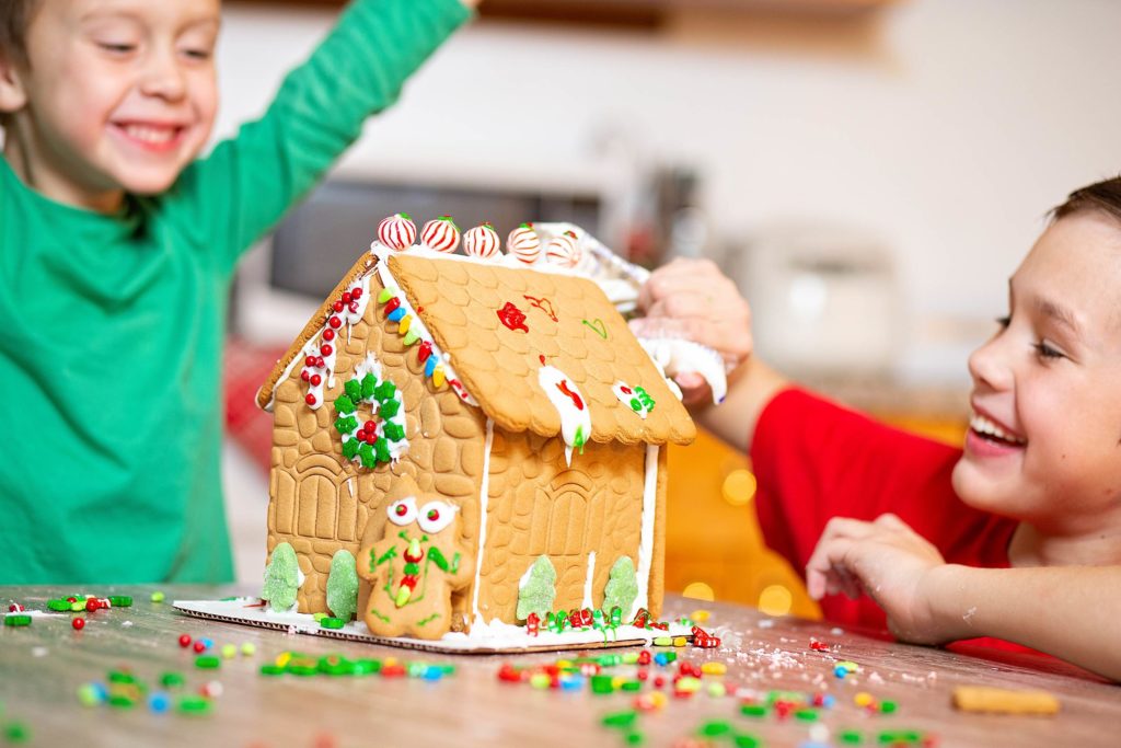 Zwei Kinder gestalten in der Adventszeit ein Lebkuchenhaus.
