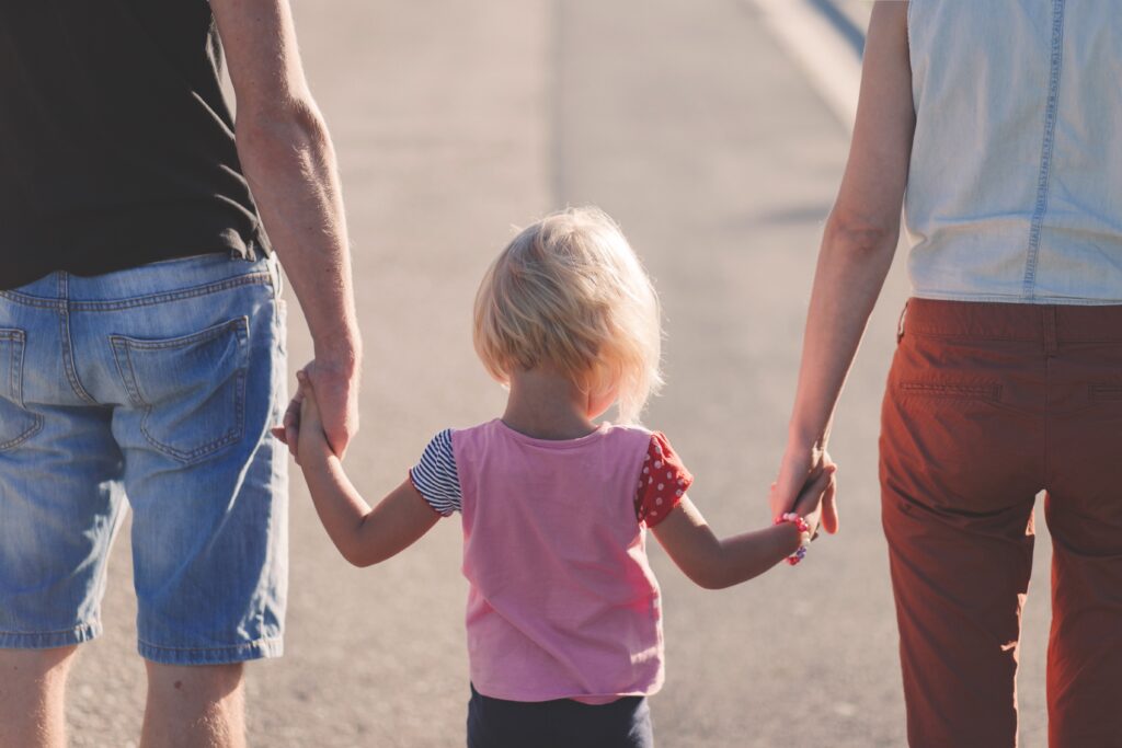 Eltern gehen mit Kind an der Hand die Straße entlang, während die Eltern über das Thema Trennung mit Kindern nachdenken