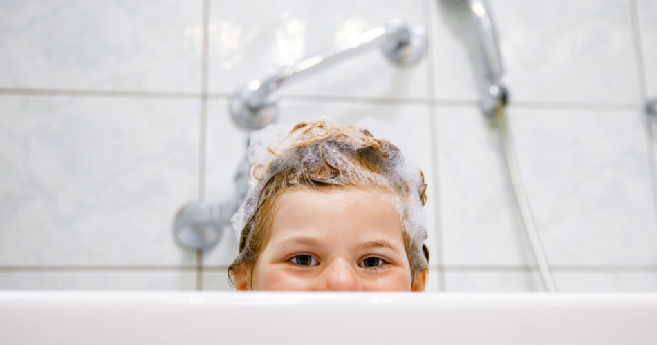 Ein süßes Kind liegt in der Badewanne und schaut über den Rand hervor.