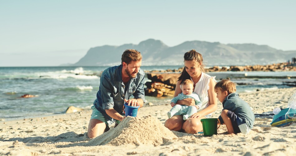 Eltern bauen mit ihren Kindern eine Sandburg auf dem Strand auf.