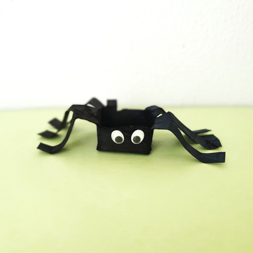 Kinder basteln eine Spinne aus einer Klopapierrolle zu Halloween