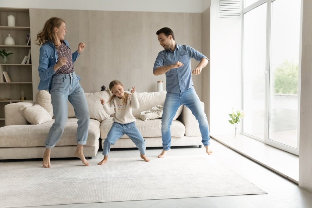 Mutter, Vater und Tochter tanzen im Wohnzimmer.