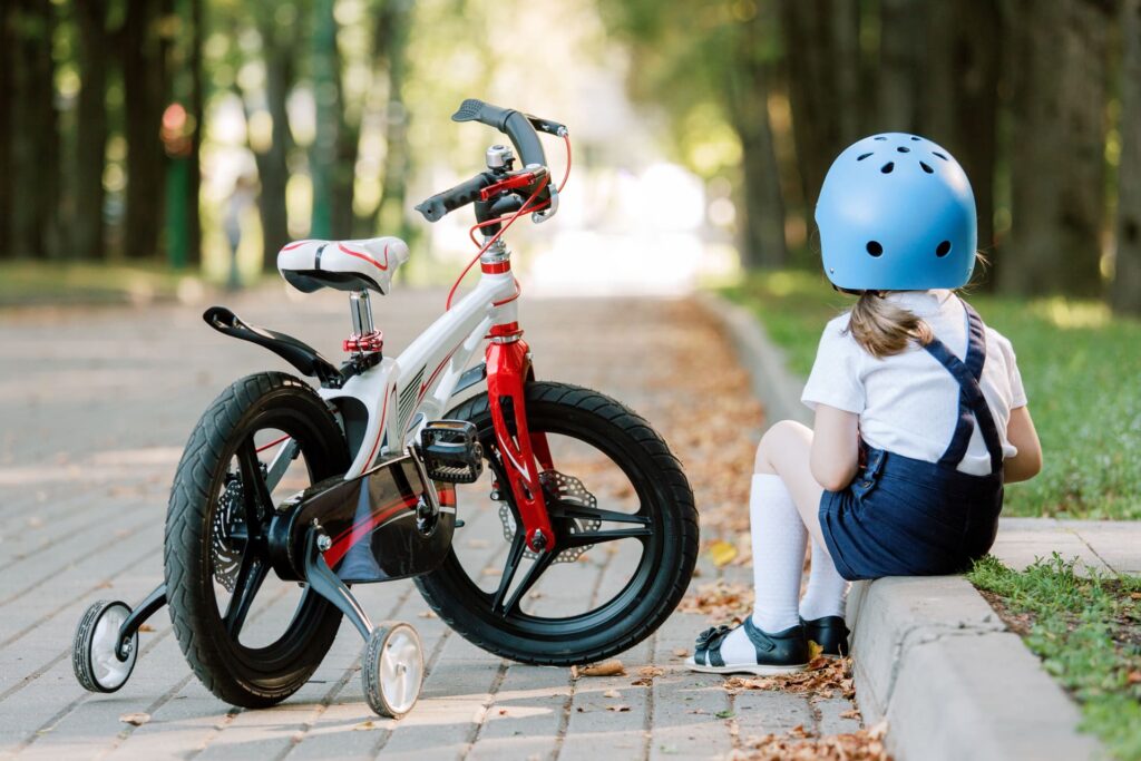 Ein Kind sitzt neben seinem Kinderfahrrad mit Stützrädern.