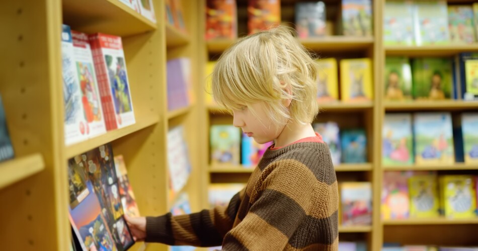 Ein kleiner Junge schaut sich Comics am Regal für Kinder an.