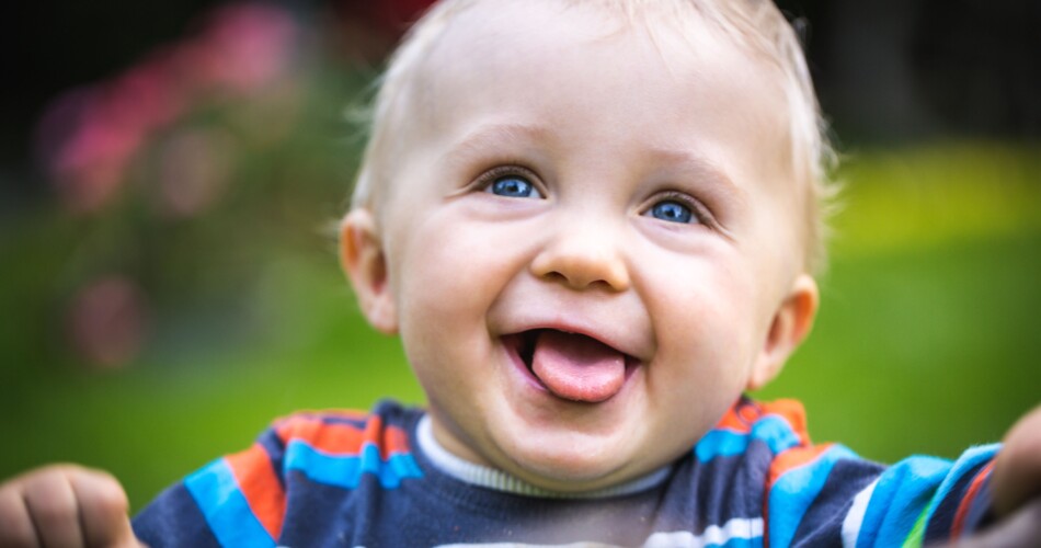Ein Kleinkind lächelt in die Kamera und streckt dabei die Zunge aus.